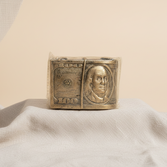 Bronze sculpture of a one hundred dollar bill on a beige fabric background