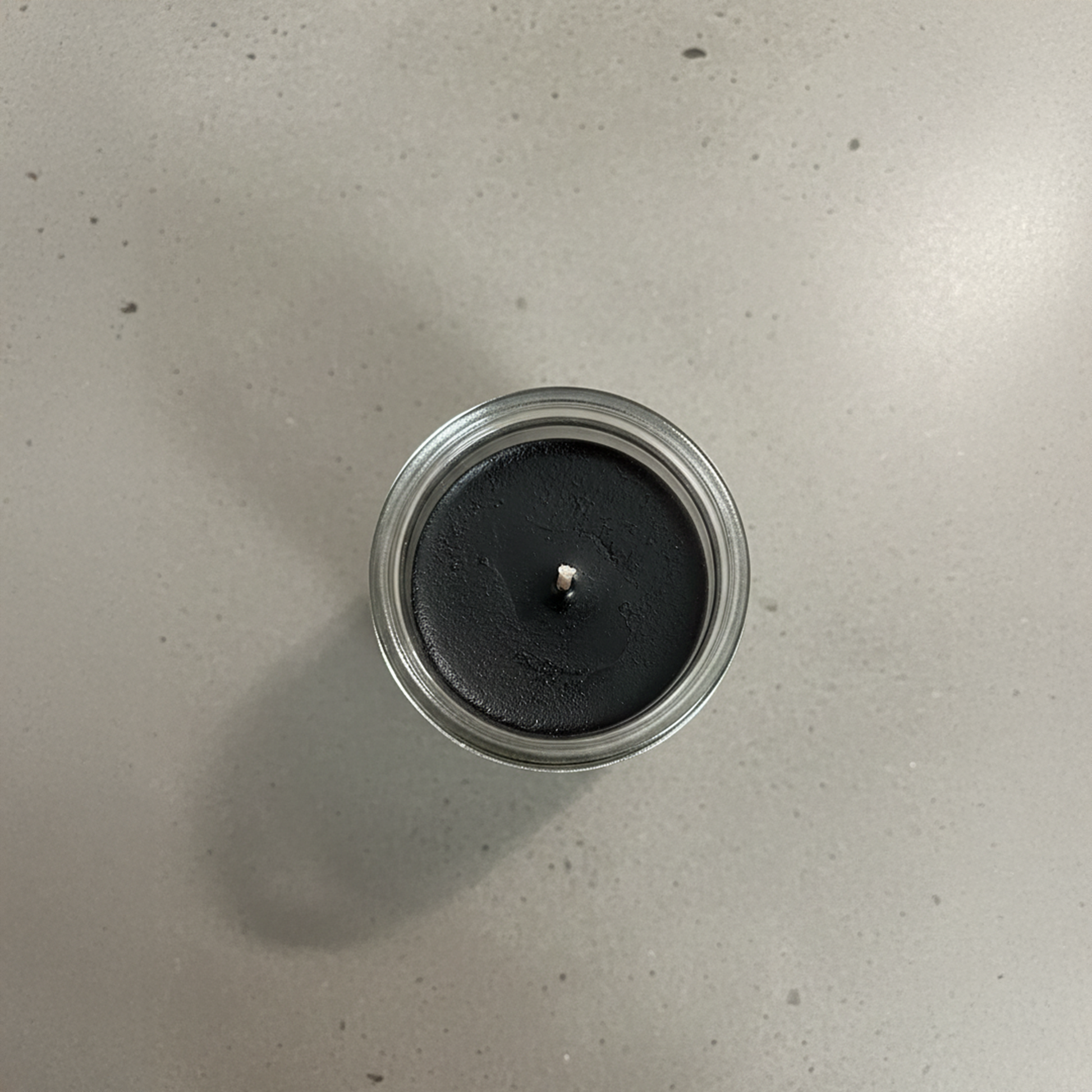 Black candle in a glass jar on a light gray surface