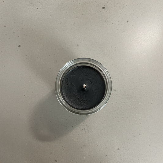 Black candle in a glass jar on a light gray surface
