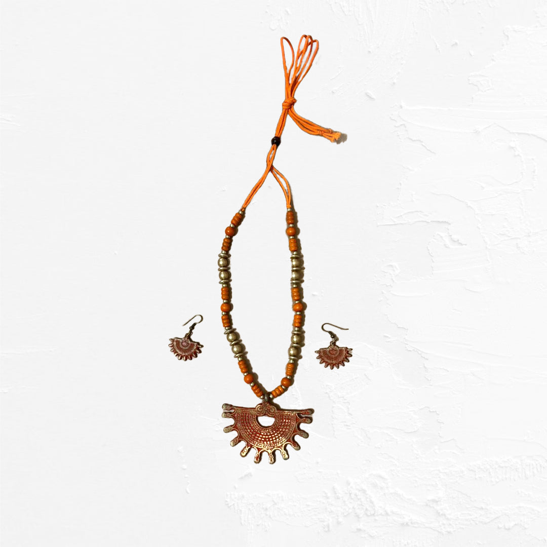 An artisan jewellery set with a vibrant orange beaded necklace, featuring a fan-shaped amulet and matching dangle earrings with a textured finish.