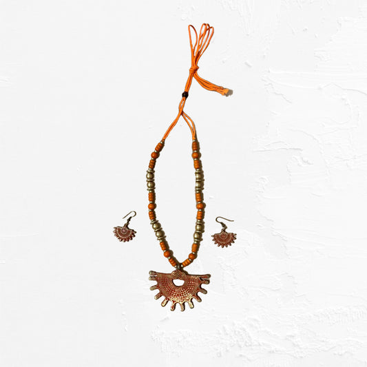 An artisan jewellery set with a vibrant orange beaded necklace, featuring a fan-shaped amulet and matching dangle earrings with a textured finish.