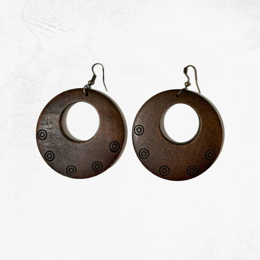 A pair of large, circular tribal wooden hoop dangle earrings with a dark finish and etched circle patterns, on a white background.