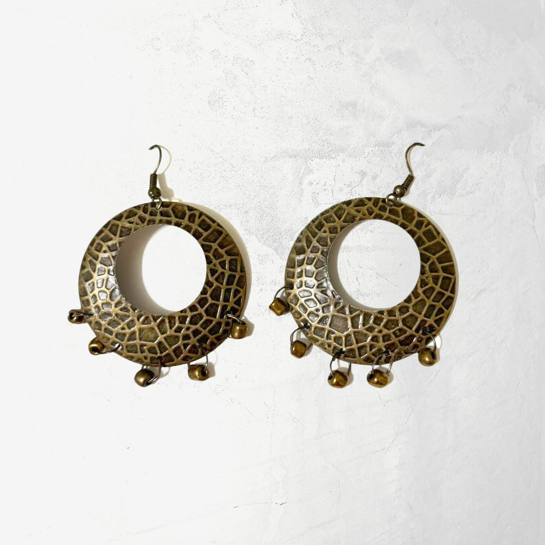 A pair of rustic textured metal hoop earrings with a dappled finish and dangling bronze-toned beads on a white background.