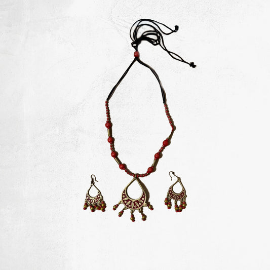 A bohemian jewellery set featuring a red beaded necklace with a golden filigree teardrop pendant and matching dangle earrings, on a white background.