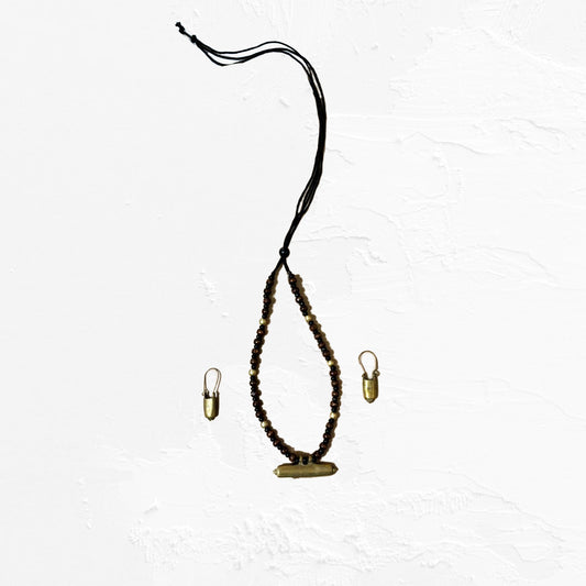 A rustic tribal jewelry set featuring a dark beaded necklace with a central aged brass-toned cylindrical pendant and matching capsule-shaped dangle earrings.